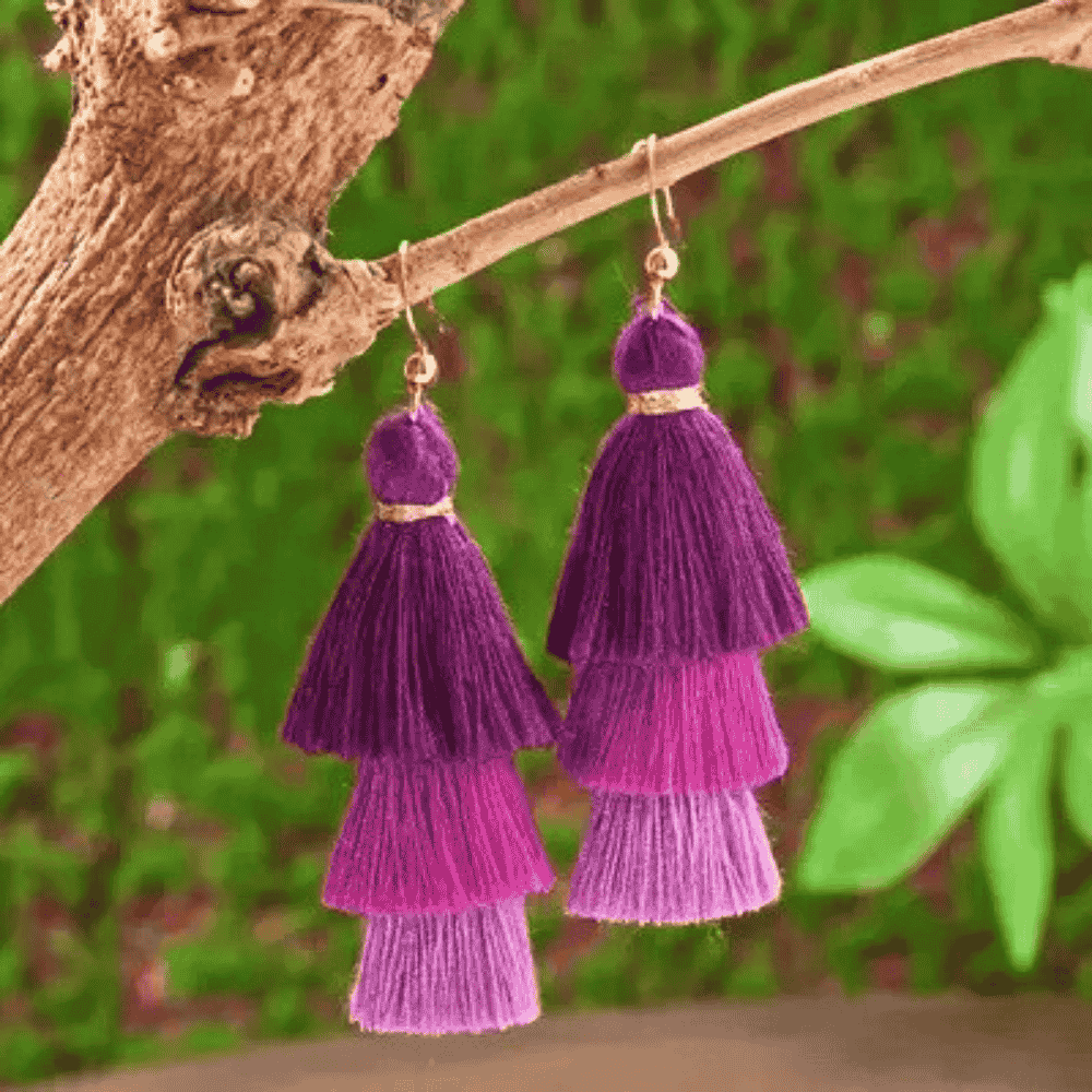 Purple tiered tassel earrings on a wooden surface with a blurred green background