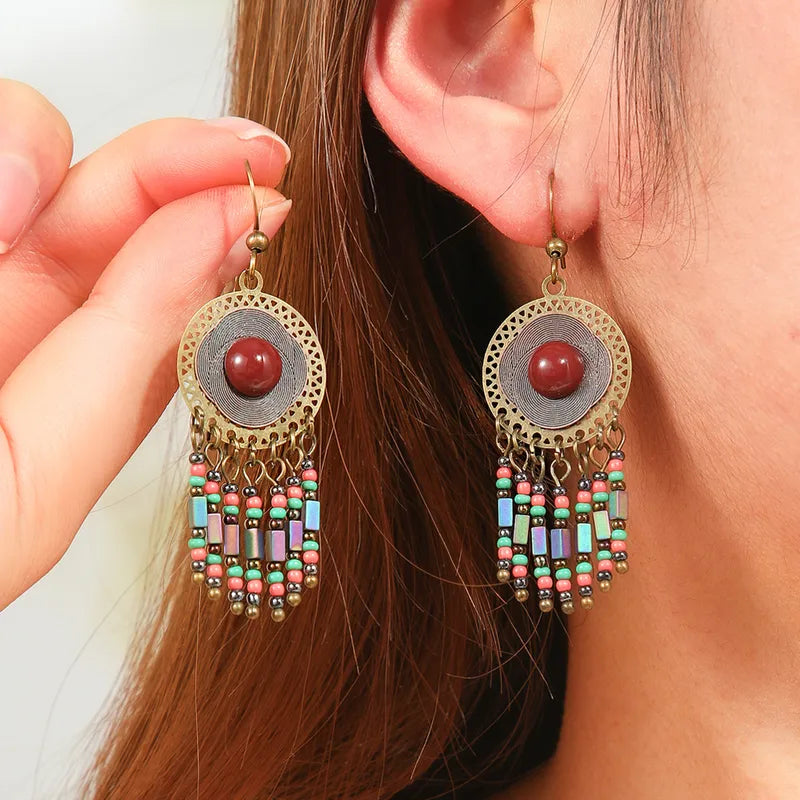 Earrings with beads and a red stone held up to an ear.