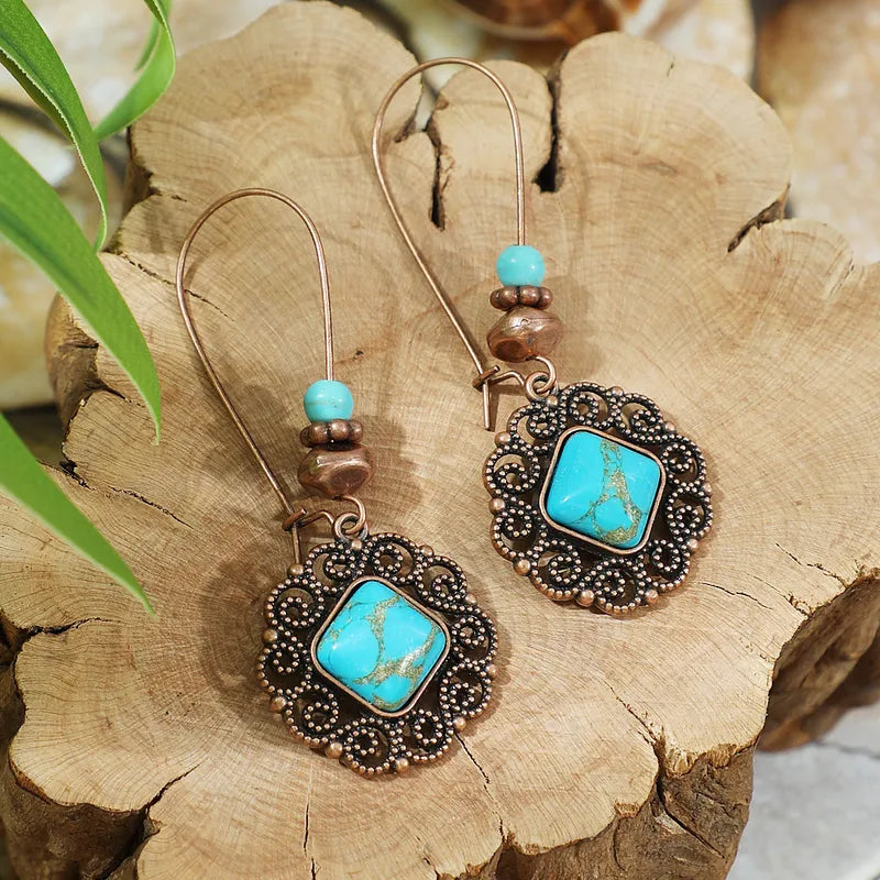 Turquoise and bronze earrings on a wooden surface with green leaves.