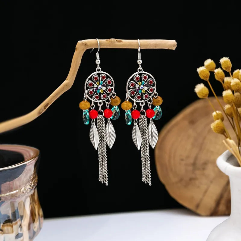 A pair of ethnic chain earrings with vibrant red stones and metalwork displayed on a wooden branch.
