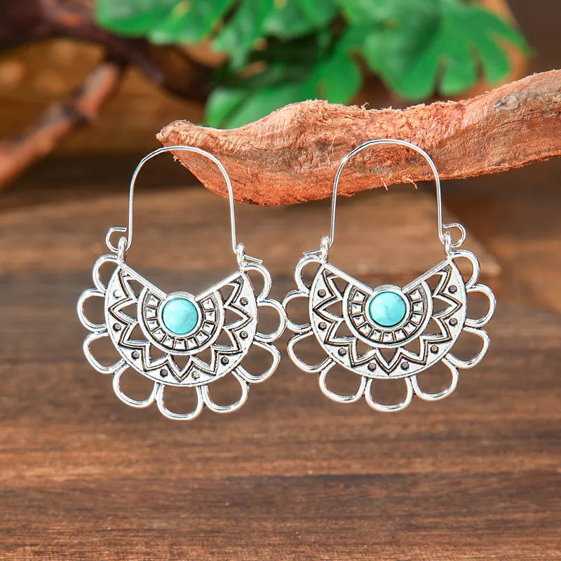 Pair of oxidised silver fan-shaped dangle earrings with a central round turquoise stone, hanging against a wooden background 