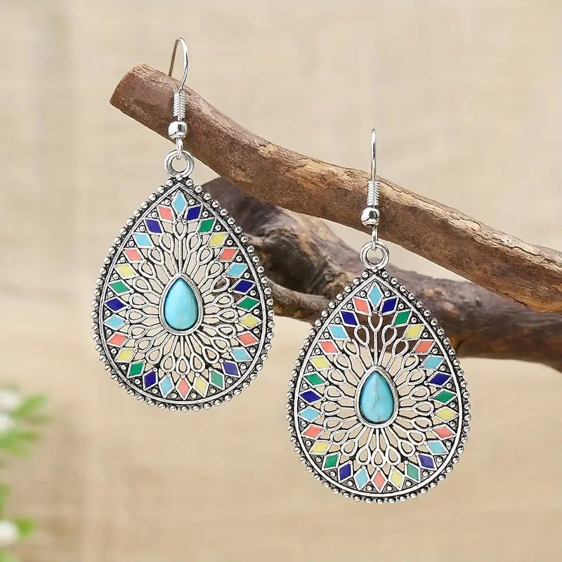 Close-up of the top part of the left silver-tone earring hook hanging from a rustic wooden branch against a blurred green bac