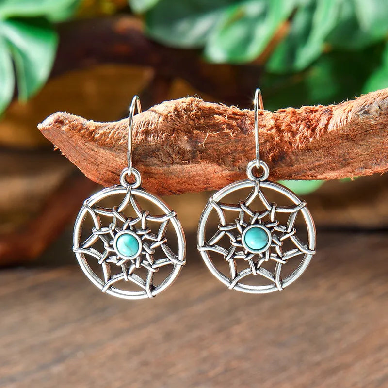 Pair of round oxidised silver drop earrings with central turquoise stone, hanging from a rustic wooden branch with green leav