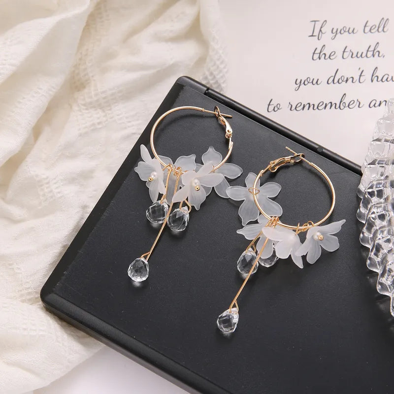 Gold hoop earrings with floral and crystal details on a black surface.