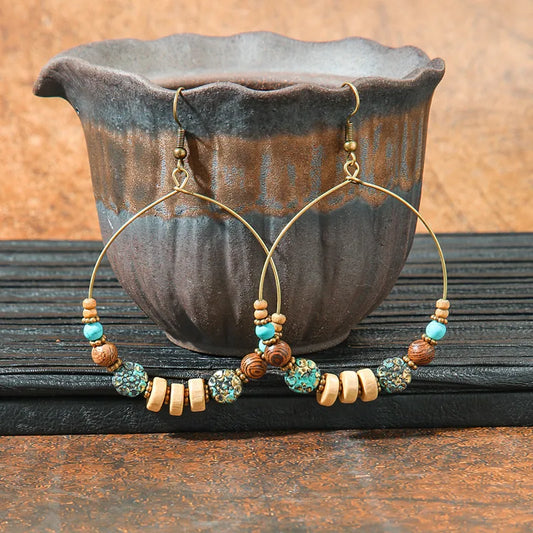 Pair of beaded hoop earrings on a wooden surface with a ceramic pot in the background