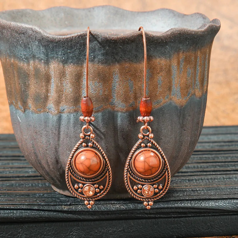 Pair of ornate earrings with orange beads against a rustic background