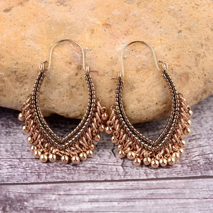 Pair of gold hoop earrings with bead details on a stone and wooden surface