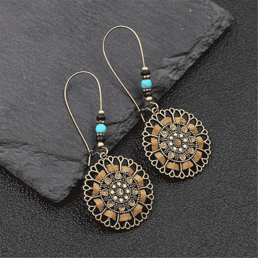 Pair of ornate earrings with intricate designs on a dark stone surface