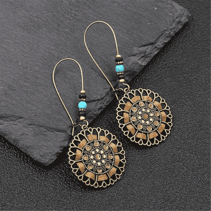 Pair of ornate earrings with intricate designs on a dark stone surface