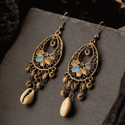 Ornate earrings with intricate designs and shell-like elements on a dark surface