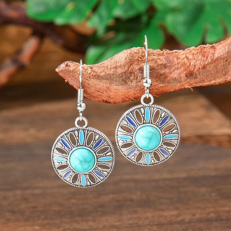 Pair of oxidised silver turquoise dangle earrings with blue enamel detailing, hanging from a rustic tree branch against a blu