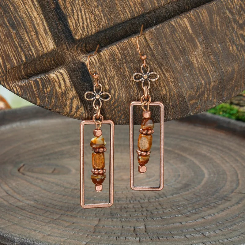 Close-up of a single oxidised antique dangle earring with rectangular frame, beaded details, and floral ear hook - Detail vie
