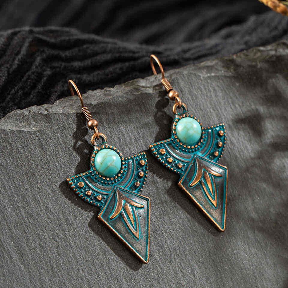 Pair of antique turquoise drop earrings with oxidised metal and tribal patterns, displayed on a dark grey surface with black 